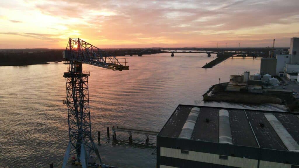 Drone video luchtfotografie van industrieel terrein met kraan bij zonsondergang over water in Midden-Nederland